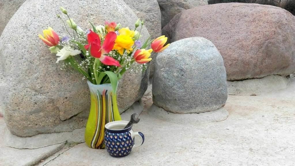 Blumen in Vase und Kaffeetasse mit Schraubenschlüssel vor Findlingsbrunnen in Dresden-Gruna